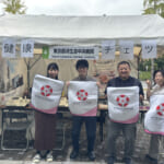 中央病院のメンバーが、済生会の紋章であるなでしこの花が描かれた布をもって、出展場所の前で集合している写真