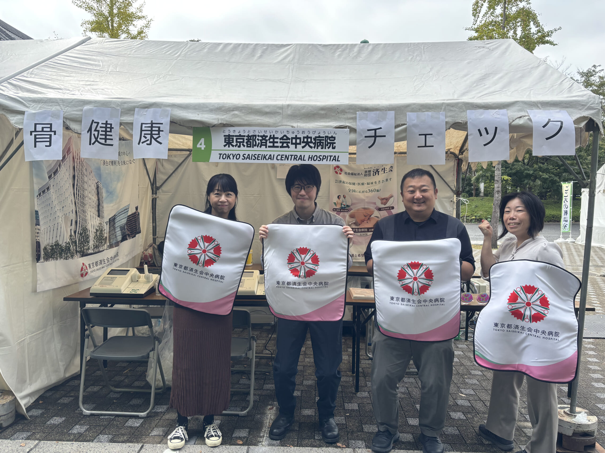 中央病院のメンバーが、済生会の紋章であるなでしこの花が描かれた布をもって、出展場所の前で集合している写真