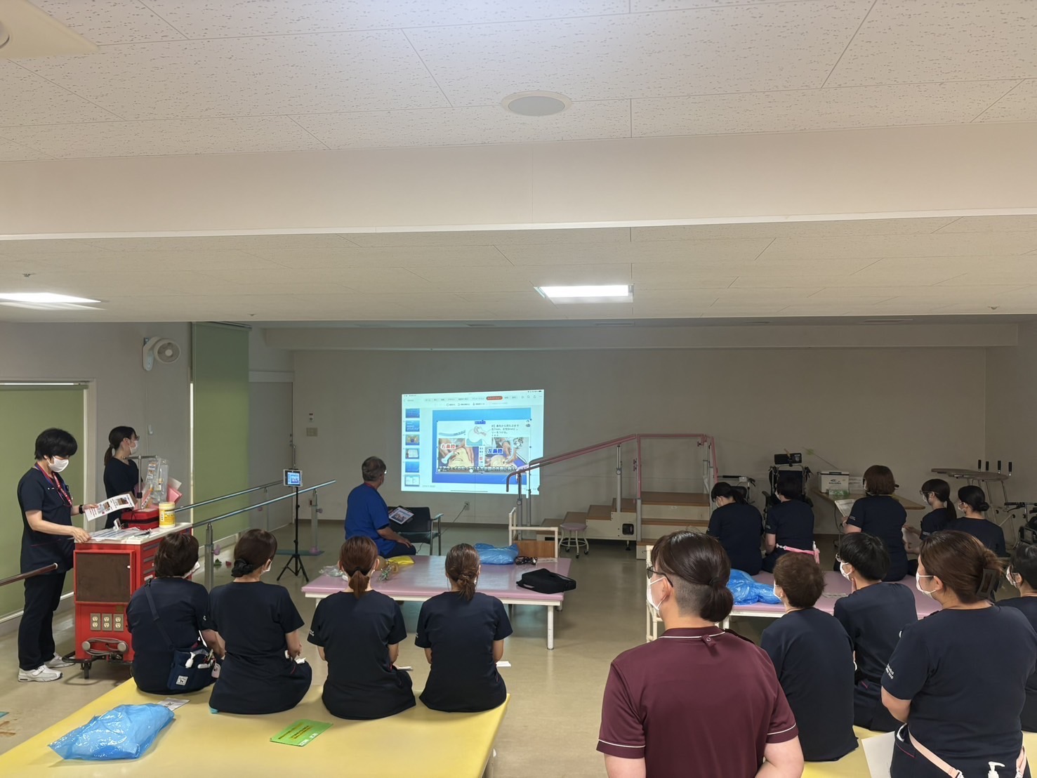 村田浩人副院長がスライド資料を用いて、患者急変時対応を説明し、参加者が聞いている写真