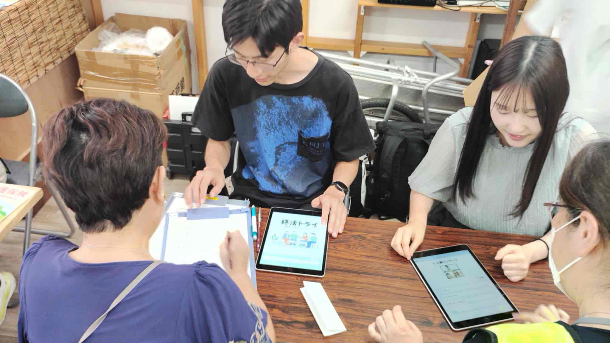 終活支援アプリ「終活トライ」を体験する来場者を、千葉工大の学生がサポートしている様子の写真