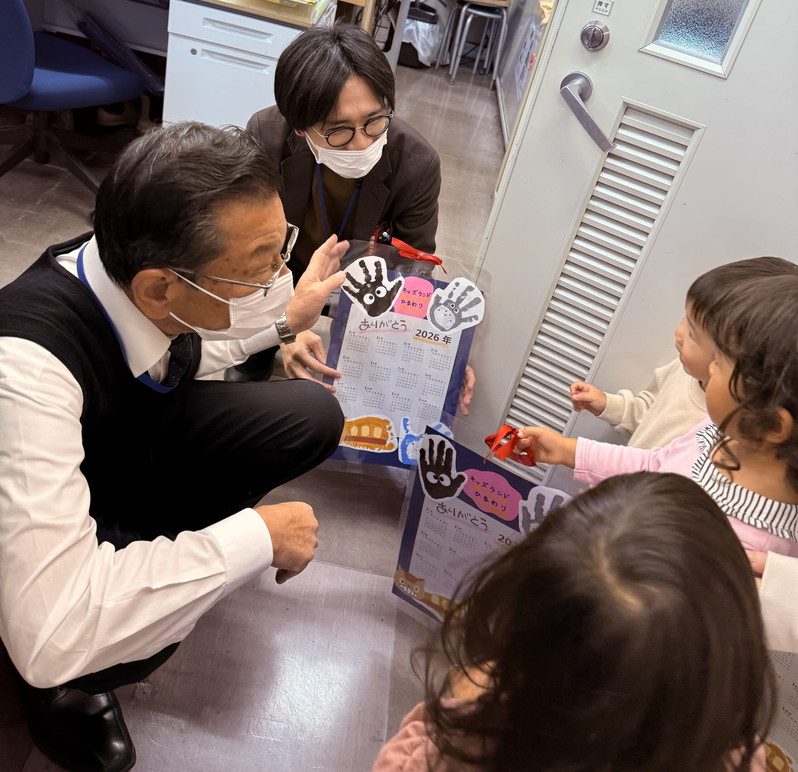病院職員が保育園の子どもから手作りカレンダーを手渡されている写真