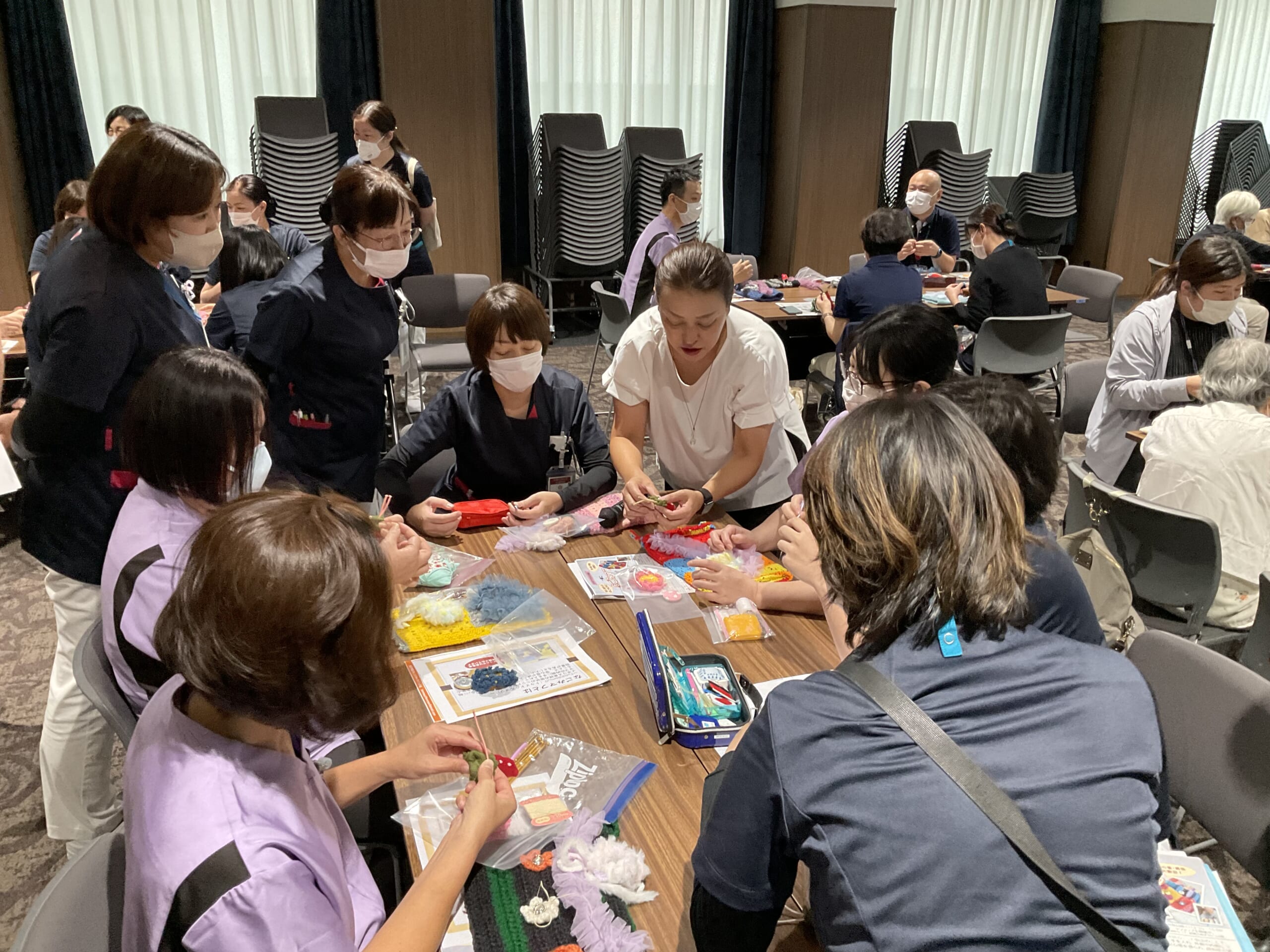 職員とボランティア達が和気あいあいと机を囲んで、認知症マフを製作している写真
