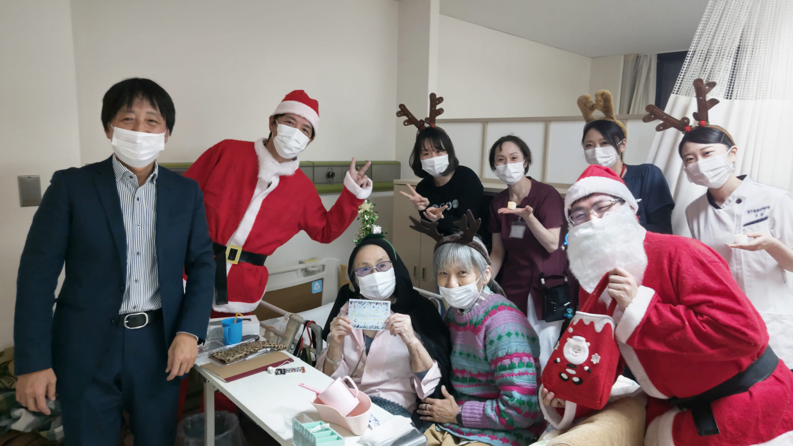 病棟での患者さんとその家族、サンタやトナカイに扮した職員の記念写真