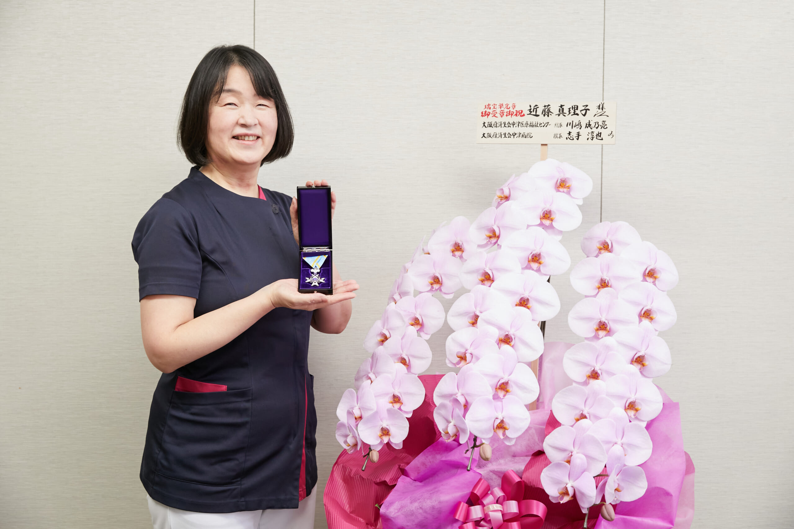 近藤真理子看護部長がお祝いにもらった胡蝶蘭の近くで勲章をもっている写真